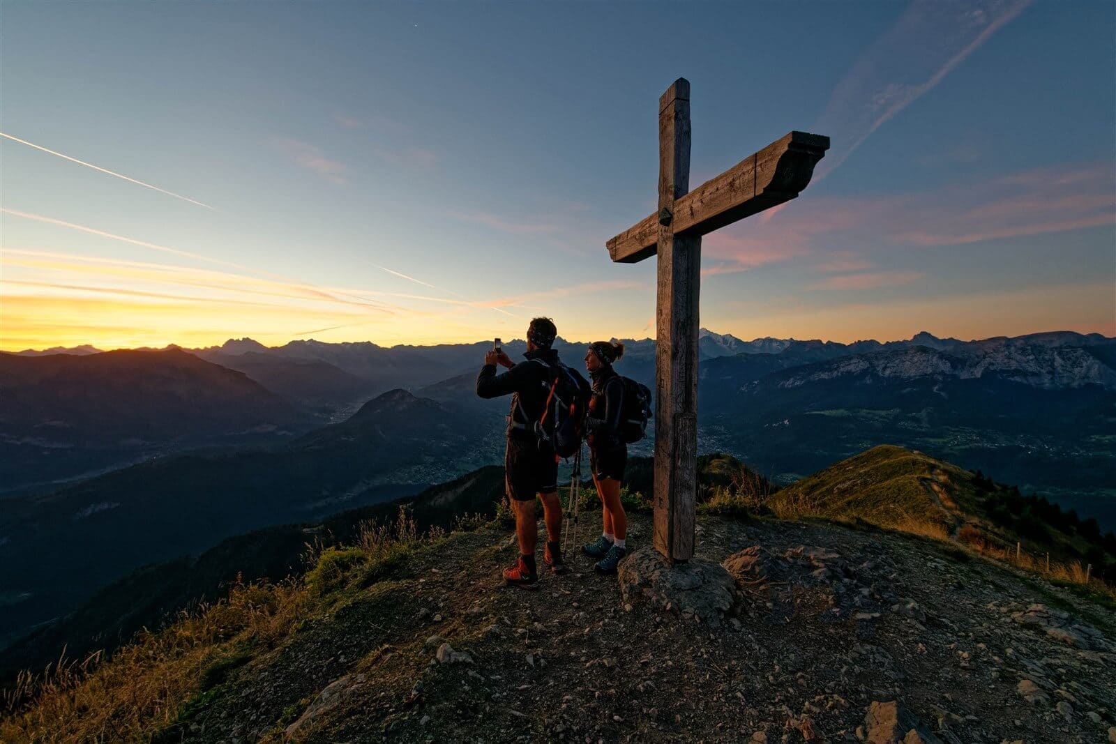 Montagnes au loin avec deux randonneurs qui prennent en photo le paysage